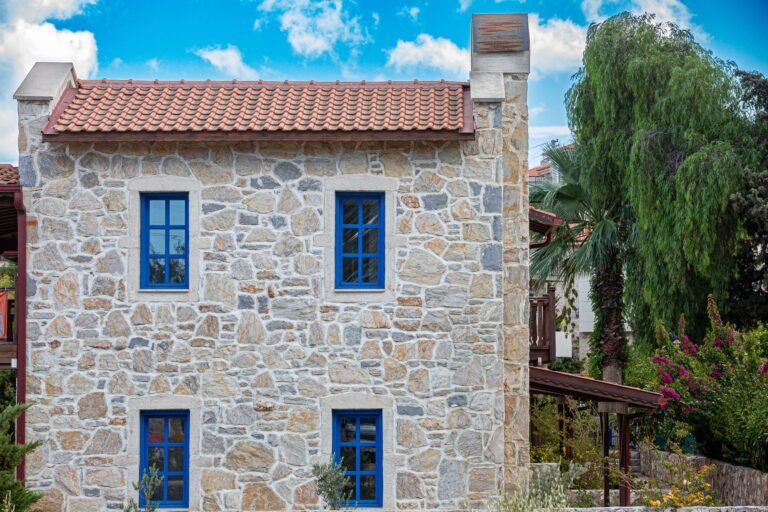 A picturesque stone house with blue windows nestled among lush greenery, perfect for architectural inspiration.